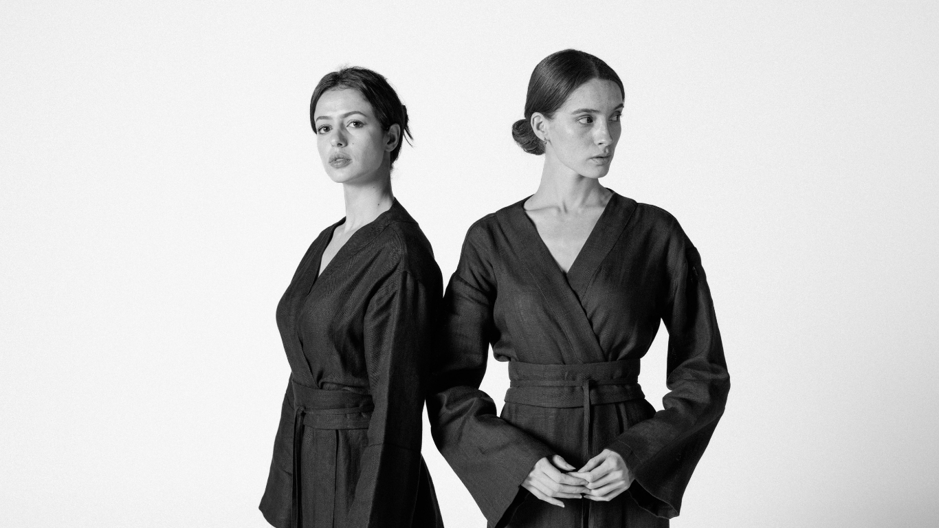 Two models in black and white wearing Atelier Mizuni linen kimonos, reflecting minimalist elegance and eco-chic style for 2025.