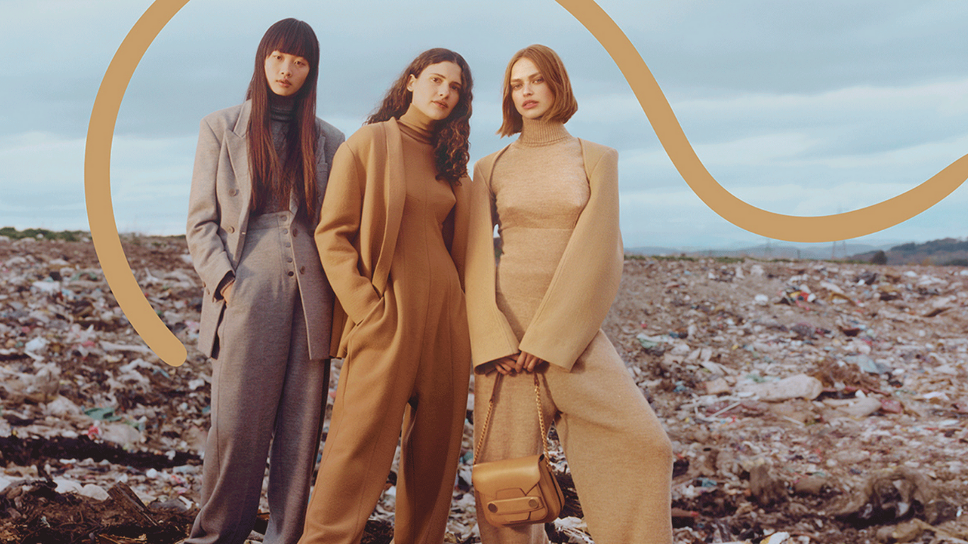 Three models in luxury clothing posing in front of a landfill, emphasizing recycling and eco-luxury as a 2025 fashion trend.