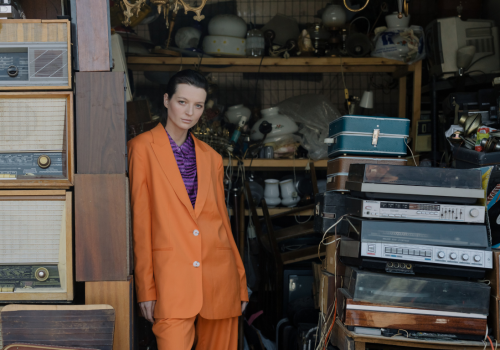 Woman in an orange vintage-style suit posing in front of an old-school shop, representing the vintage fashion niche.