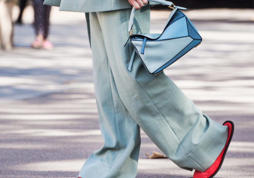 Close-up of a woman wearing classic suit pants and holding a matching modern bag.