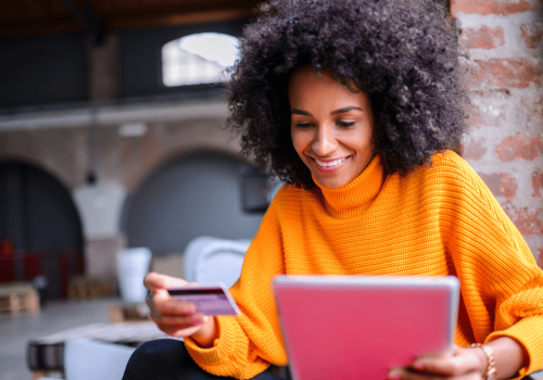 A woman holding her credit card and using her iPad to shop online for winter clothes.